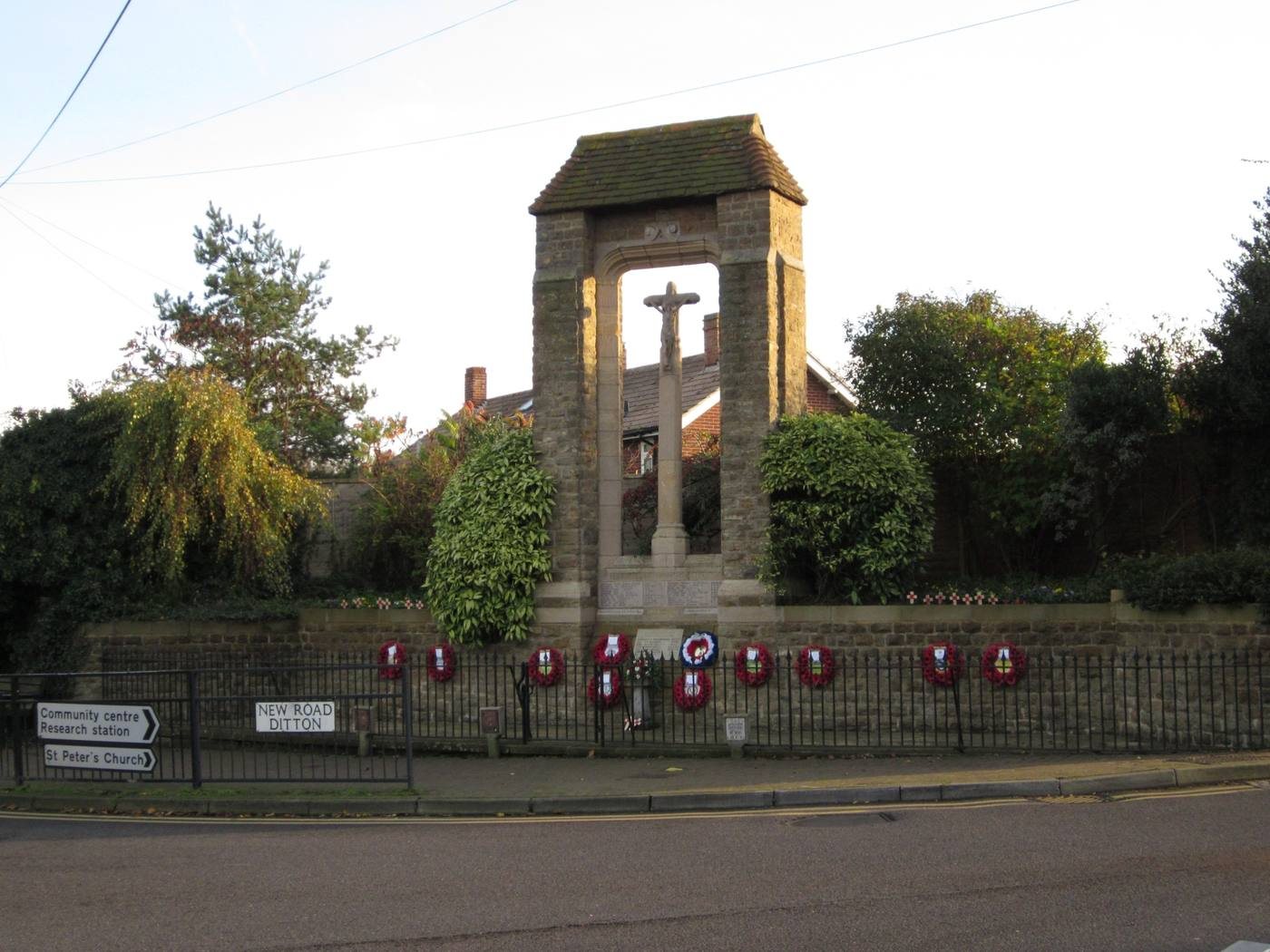 Ditton War Memorial: a tiled stone arch over a crucifix, wreaths along the railings, at the junction of New Road, Ditton